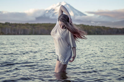 Young woman standing in lake against sky during sunset