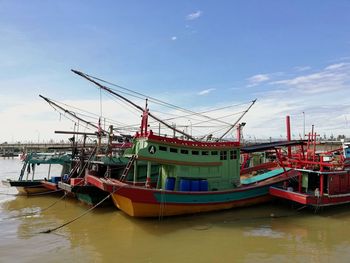 Fishing boats moored at harbor against sky