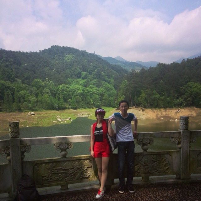 sky, mountain, leisure activity, rear view, lifestyles, full length, casual clothing, tree, water, beauty in nature, nature, scenics, railing, cloud - sky, togetherness, standing, tranquility, tranquil scene