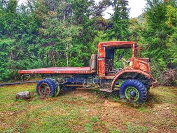 Abandoned tractor on field against trees