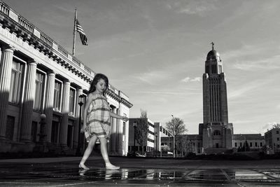 Girl walking at fountain in city against sky