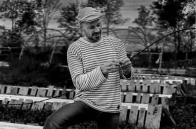 Smiling man preparing fishing bait while standing at park