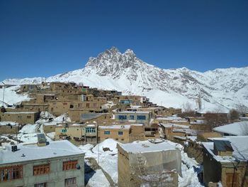 A picture of a snow covered village and mud and clay houses with snow covered mountain in background