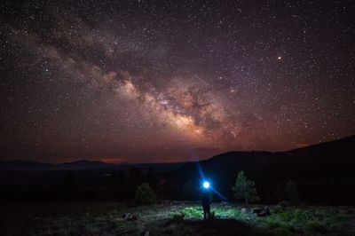 Silhouette person holding illuminated flash light against milky way at night