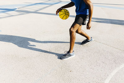 Young man dribbling basketball at sports court during sunny day