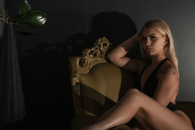 Young woman looking down while sitting against black background