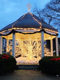 Illuminated park by building against sky at dusk