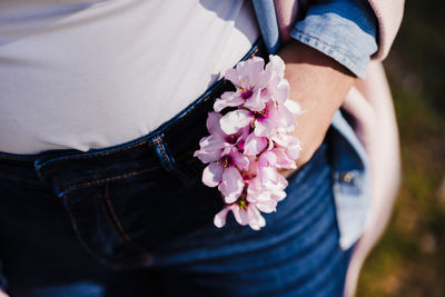 Close up of woman holding pink almond tree flowers in jeans pocket on sunny day. spring time
