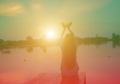 Rear view of woman standing by lake against sky during sunset