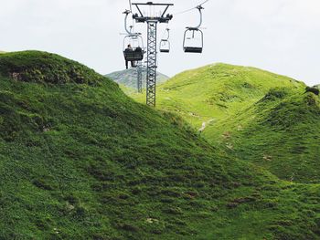 Low angle view of men sitting on ski lift over hills against sky
