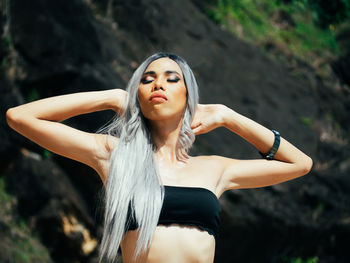 Portrait of young trans woman standing against rock