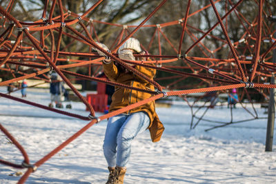 Full length of woman climbing on ropes at snow covered park