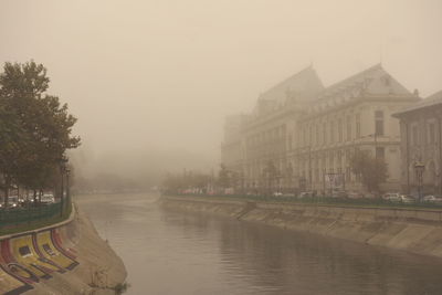Buildings by river in city against sky