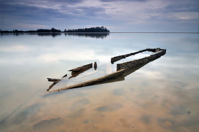 Abandoned boat in lake against cloudy sky