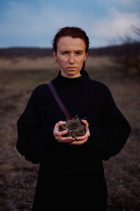 Portrait of young woman standing on field and holding a bird's nest