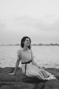 Young woman sitting on beach against sky