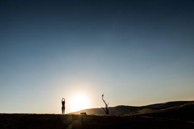 Silhouette woman standing on landscape against sky during sunset