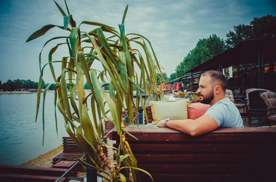 Portrait of man sitting by plants against sky