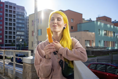 Portrait of young woman standing against buildings in city