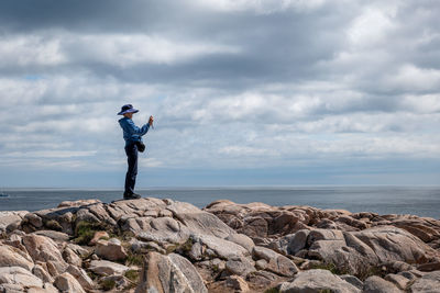 Side view of man standing on rock by sea against sky