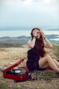 Young woman lies in nature in a black dress next to an old gramophone and listens to music