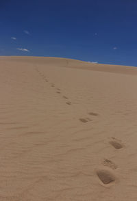 Footprints on sand at beach against clear blue sky