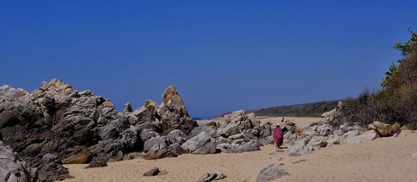 Rear view of woman standing on rock against clear blue sky