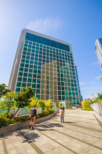 Low angle view of people walking on modern building against sky