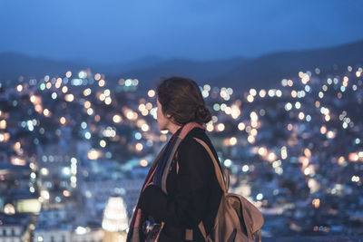 Rear view of woman in city against sky at night