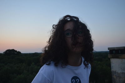 Beautiful young woman wearing sunglasses against clear sky during sunrise