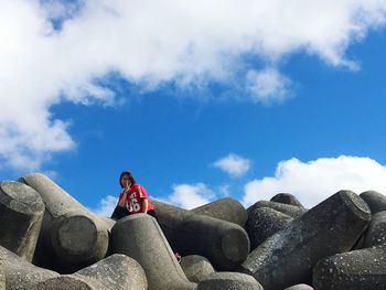 Low angle view of woman sitting on rock against sky