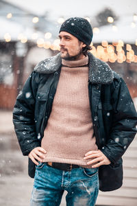 Young man looking away while standing in snow