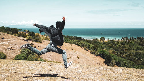 Full length of happy man jumping on field with sea in background