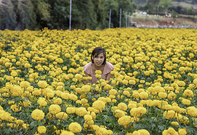 Portrait of smiling woman sitting against yellow flowers