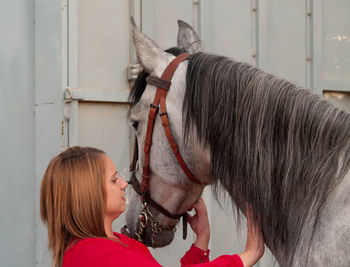 Young woman touching horse while standing metal built structure