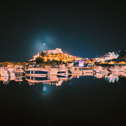 Illuminated buildings by sea against sky at night