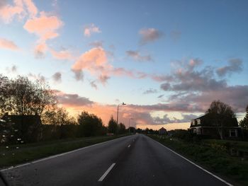 Road by trees against sky during sunset