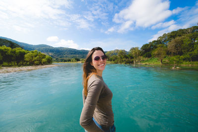 Portrait of smiling young woman in lake against sky