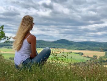 Woman sitting on field against sky