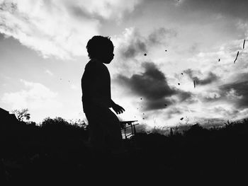 Silhouette boy standing on field against sky