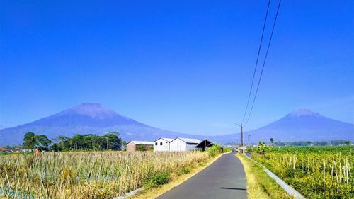 Road leading towards mountains against clear blue sky