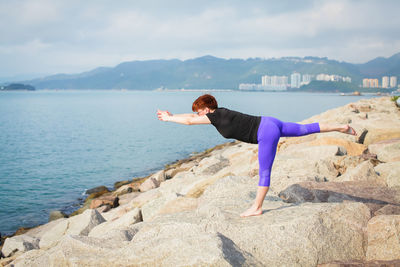 Full length of mature woman practicing yoga on rocks at beach