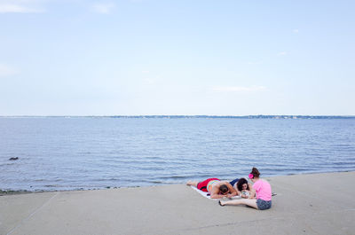 Women sitting on shore at beach against sky