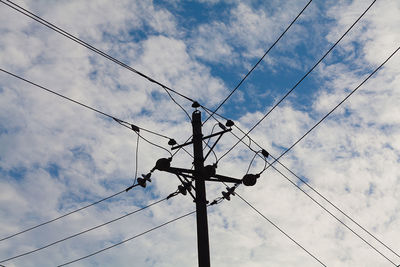 Low angle view of electricity pylon against cloudy sky