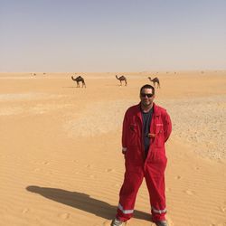 Full length portrait of man standing with camels in background against clear sky