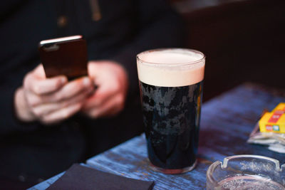 Midsection of man using phone while sitting by beer glass on table