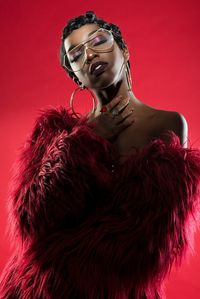 Young woman wearing eyeglasses and fur clothing standing against red background