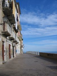 Footpath amidst buildings against blue sky