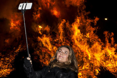 Woman taking selfie against bonfire at night