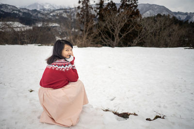 Portrait of woman crouching on snow covered land